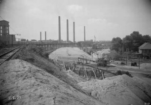 Industrie-Kraftwerk. Aufschüttung des neuen Bahndammes der Grubenbahn für die Kohlezufuhr, daneben aufgeständerte alte Trasse. Blick auf Werkanlagen mit Schornsteinen : Lauta (Niederlausitz). Industrie-Kraftwerk. Aufschüttung des neuen Bahndammes der Grubenbahn für die Kohlezufuhr, daneben aufgeständerte alte Trasse. Blick auf Werkanlagen mit Schornsteinen