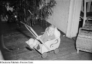Porträt eines kleinen Mädchens mit Puppenwagen vor einem Weihnachtsbaum