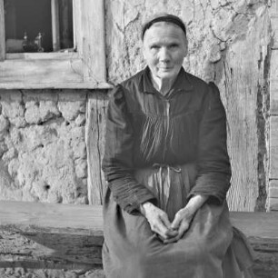 Strohgedecktes Blockhaus in Burg-Kauper. Frau Nowick in Spreewälder Alltagstracht vor ihrem Gehöft. : Ze słomu skryte kładźity twar statoka w Kupaŕskich Bórkowach. Knjeni Nowickowa we wšědnej Błótowskej drasće před swojim statokom.