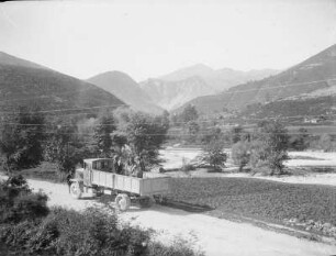 Lastwagen mit Lasttier : Ein Lastwagen auf einer Landstraße in einem Bergtal, mit Personen und Lasttier auf der Ladefläche