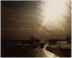 Blick auf eine Straße in der Dämmerung mit der Spiegelung der Sonne auf dem Autofenster, aus dem das Foto aufgenommen wurde (Altersgruppe 14-1)7