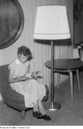 Junge Frau neben einer Stehlampe, eine Zeitung lesend