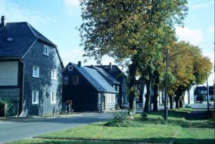 breite Straße mit Grünstreifen und Bäumen; Häuserzeile