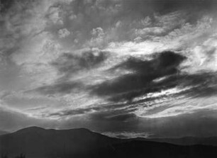 Wolkenbilder. Dunkle Wolken vor untergehender Sonne über Berglandschaft