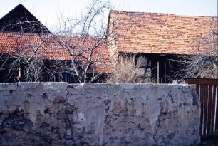 Grundstücksmauer, dahinter Obstgarten und Dächer von Gebäuden