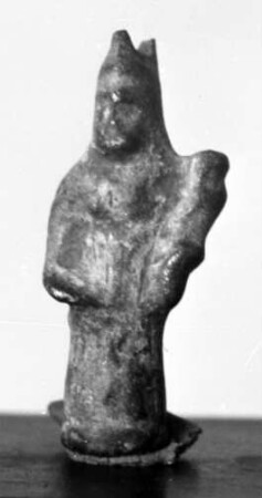 Kleines Amulett in Form eines langbekleideten Figürchens, das in der Linken einen großen unkenntlichen Gegenstand trägt, Öse am Kopf