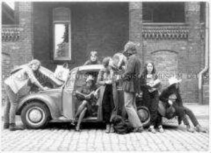Eine Gruppe von Menschen an und um einen VW-Käfer herum