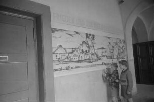 Dekorative Ausgestaltung der Klassenräume und Schulflure in der Einheitsschule Baumschulenweg und Oberschule Niederschöneweide in Vorbereitung des Deutschlandtreffens der Jugend für Frieden und Völkerfreundschaft zu Pfingsten 1950 : Schüler beim Anbringen eines Plakats zum Deutschlandtreffen an einer Wand im Hausflur einer Schule
