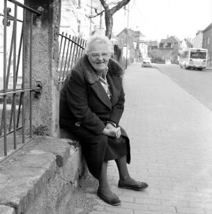 Elfriede : Colditz. Portrait einer alten Dame auf einem Mauersims an der Straße