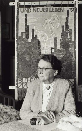Loschwitzer Porträts. Die Textilkünstlerin Margarete Freytag-Just auf einer Veranda vor Wandteppich "Und neues Leben blüht..." (bez. 1965)