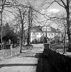 Grönwohldhof: Gutshaus: vorn rechts und links Mauer aus behauenen Feldsteinen mit schmiedeeisernem Tor und zwei Figuren: dahinter Parkanlage mit Bäumen