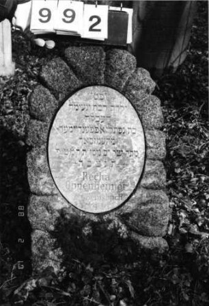Grabstein 992 (Index: 99804006) Material: Marmorplatte in Naturstein Zustand: gut Maße HxBxT: 80x46x25 cm Beschreibung: Stele mit Flachbogenabschluß und Inschriftenplatte Symbolik: florale Verzierungen der Inschriftenplatte: Grabstein 992