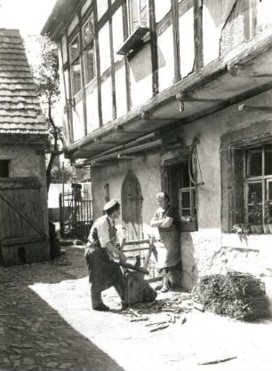 Bauernhof. Holz hackender Mann und ihm dabei zusehende Frau
