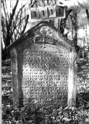 Grabstein 1111 (Index: 99753267) Material: Sandstein Zustand: leicht verwitt/Stele eingesunken Maße HxBxT: 95x68x12 cm Beschreibung: Stele, giebelartiger Abschluß, Schriftfeld eingetieft Symbolik: Blüte?, Schriftband: Grabstein 1111