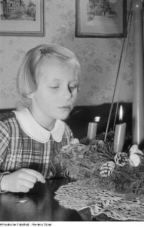 Ein Mädchen bläst gegen die Flamme einer Kerze eines Adventskranzes