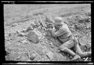 Übungsgelände I bei Mouzon (Dep. Ardennes, Frankreich): Soldat mit Stahlhelm und umgegürtetem Langmesser im Graben liegend beim Zielen mit dem Gewehr (Rückansicht, Nahaufnahme) ("im Trichter")