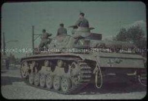 Deutsche Soldaten auf einem Panzer in einer Ortschaft