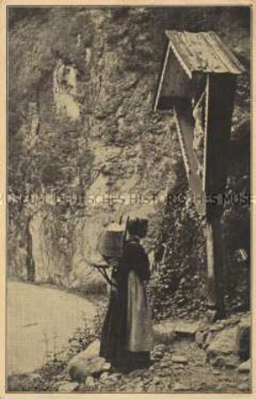 Frau vor Kruzifix im Gebirge