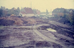 Lübecker Straße: Abrissgrundstück für neues Postgebäude mit Erdhaufen und Wasserloch: hinten links Bagger: hinten Wohnhäuser: hinten Mitte Schornstein der Stadtwerke und Gebäude