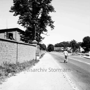 Möllner Landstraße: rechts Bushaltestelle: daneben Fußgänger beim Überqueren der Straße: dahinter Einmündung der Bahnhofstraße: im Hintergrund Wohnblocks und Geschäftsgebäude: links Gutsmauer: dahinter Scheune des ehemaligen Gutes Glinde