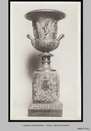 Kelchkrater mit auf Stöcken gestützten und im Kontrapost stehenden Männern sowie Weinlaub und Akanthusdekor auf einem hohem, modernen Sockel mit einem Kranz aus Lorbeer- und Eichenlaub