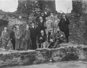 Auf Exkursion : Gruppenportrait einer Exkursionsgesellschaft in einer Ruine. Rudolf Zimmermann erster von rechts sitzend.