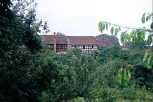 Blick über Bäume auf unterschiedliche Fachwerkgebäude und einen Schornstein