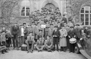Gruppenaufnahme einer Musterungsgruppe für die Wehrmacht mit Schild "Die unbekannte Waffe des Führers - Jahrgang 1905" vor dem Tuchmacherhaus