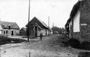 Soldat auf einem Pfad durch ein scheinbar verlassenes und teilweise zerstörtes Dorf