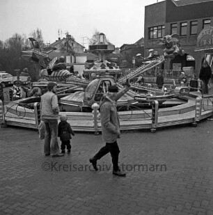 Kaufhaus Nickel: 1-jähriges Jubiläum: Heiligengeiststraße: Flohmarkt: Personen vor einem Fahrgeschäft, rechts im Hintergrund das Kaufhausgebäude