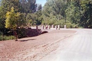 Schäperbarg: Granitquaderbrücke über die Barnitz: Sanierung: Fertigstellung: Seitenansicht: Stirnwand, Flügelwand, oben Granitpoller mit Geländer, Arbeiter: vorne Neuanlage der Böschung