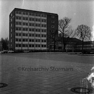 Hochhaus [später Gebäude B]: Mommsenstraße: hinten rechts Haupthaus [später Gebäude A] und Anbau mit Garagentrakt: davor Innenhof, Parkplatz und Bäume: vorn Bahnhofsvorplatz mit Busbahnhof und Fußgängerüberweg
