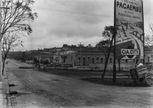 Werbeschild : Ein Schild zur Bewerbung der neuer Wohnsiedlung Pacaembú, welche heute zu São Paulo gehört. Im Hintergrund eine neue befestigte Straße mit geschlossenem Entwässerungskanal. Davor ist die Straße unbefestigt und der Graben offen.