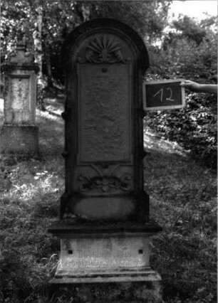 Grabstein 12 (Index: 100100941) Material: Sandstein Zustand: Schrifttafel fehlt Maße HxBxT: 170x53x24 cm Beschreibung: Stele, getreppter Sockel, Rundbogenabschluß, Schrifttafel rechteckig Symbolik: Verzierungen Besonderheit: eingravierte Nummer: 38: Grabstein 12