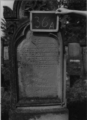 Grabstein 36 (Index: 99801869) Material: Sandstein Zustand: stark verwittert mit Textverlust, oben abgebrochen Maße HxBxT: 200x54x24 cm Beschreibung: Stele, Sockel, eingezogener Rundbogen mit Akroteren, eingetieftes Schriftfeld mit Maßwerk Symbolik: Blätterverzierungen: Grabstein 36A