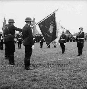 Meddewade: Freiwillige Feuerwehr Meddewade: Fahnenweihe: Festwiese: Fahnenträger mit der Meddewader Fahne und der Weihfahne des Amtes Bad Oldesloe-Land: dahinter Fahnenträger benachbarter Wehren: hinten angetretene Wehren und Zuschauer: 01.06.1974