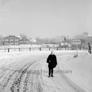 Rohlfshagener Weg / Dorfstraße: rechts Ortseingangsschild: vorn Kind: im Hintergrund Zaun und Bauernhäuser: Winter