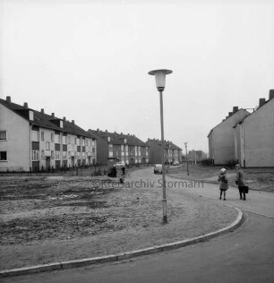 Königsberger Straße: Neubaugebiet mit Geschosswohnungsbau: vorn Mitte Straßenlampe: rechts zwei Schulkinder: hinten rechts und links mehrere Wohnblocks: hinten Mitte parkende Pkws und mehrere Personen