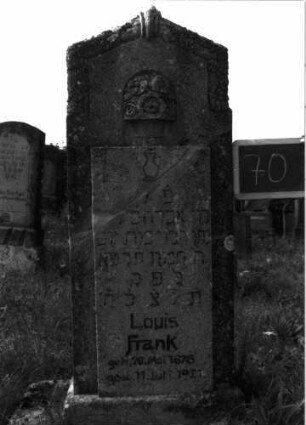 Grabstein 70 (Index: 100100726) Material: Kalkstein Zustand: verwittert Maße HxBxT: 127x46x18 cm Beschreibung: Stele, Sockel, giebelartiger Abschluß, vorstehende Schriftplatte Symbolik: Levitenkanne, Blumenbordüre um den Abschluß, Blumen über der Schriftplatte: Grabstein 70