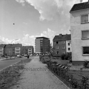 Stonsdorfer Weg: mittig parkende Pkws, Wohngebäude an den Seiten, im Hintergrund das Rathausgebäude: Blick Richtung Westen