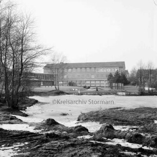 Mittelschule (Gemeinschaftsschule) Harksheide: vorne Baustelle des späteren Teiches, dahinter Robbenstatue und Person am Teichrand, dahinter Schulgebäude: Blick nach Westen