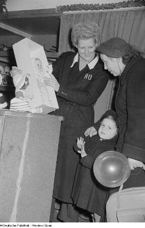 Eine Verkäuferin im Handelsorganisation-Kaufhaus präsentiert einer Frau und einem Kind eine Puppe