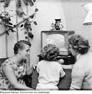 Zwei Frauen mit Kind vor laufendem Fernsehgerät sitzend