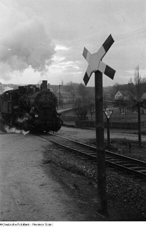 Zug mit Dampflokomotive überfährt einen unbeschrankten Bahnübergang mit Andreaskreuz