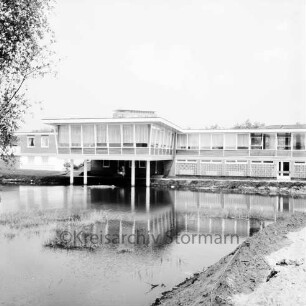 Am Exerzierplatz: Sportlerheim, links davon das Hausmeisterwohnheim, im Hintergrund das Rathausgebäude, vorne ein Teich: Blick von Südwesten
