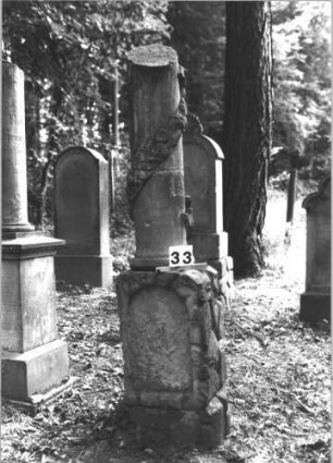 Grabstein 33 (Index: 99898747) Material: Sandstein Zustand: stark verwittert Maße HxBxT: 102x45x20 cm Beschreibung: aufgesockelte Stele mit Konvexbogenabschluss, oben mit Palmette und Voluten Symbolik: Palmette, Voluten: Grabstein 33