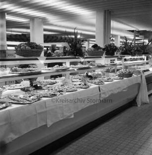 Peters Delikatessen: Mühlenstraße, Ecke Hindenburgstraße: Feinkostgeschäft: 50-jähriges Firmenjubiläum, gleichzeitig Betriebsübergabe: Innenaufnahme: Verkaufsraum: Buffet, Platten mit Speisen auf Tischtüchern: Blumenschmuck