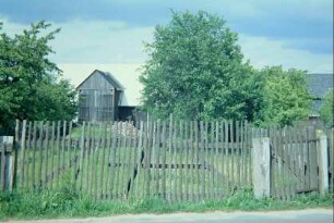 Garten am Dorfrand mit Staketenzaun, hinten Scheune mit Hochfahrt