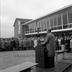 Am Exerzierplatz: Mittelschule (Gemeinschaftsschule) Harksheide: Einweihung: Bürgermeister Carl Lange hält eine Rede, dahinter Gäste vor dem neuen Schulgebäude