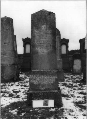 Grabstein 2 (Index: 100114992) Material: ? Zustand: gut Maße HxBxT: 168x48x22 cm Beschreibung: Stele auf gestuften Sockel, Spitzgiebel mit Davidstern Symbolik: Davidstern: Grabstein 2